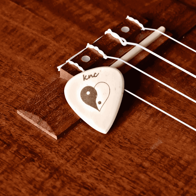 A handmade custom bone guitar pick featuring an engraved black and white Yin Yang logo