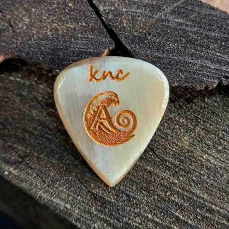 The official Ali Özen Signature Pick by Knc Picks, showing the artist's signature engraved on the 2.5mm natural horn pick.