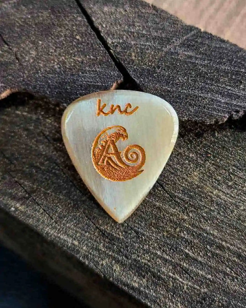 The official Ali Özen Signature Pick by Knc Picks, showing the artist's signature engraved on the 2.5mm natural horn pick.