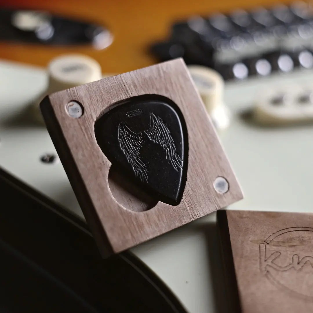 Close-up macro detail of the Angel Wings engraving on the polished, pure black surface of a natural ebony wood pick.