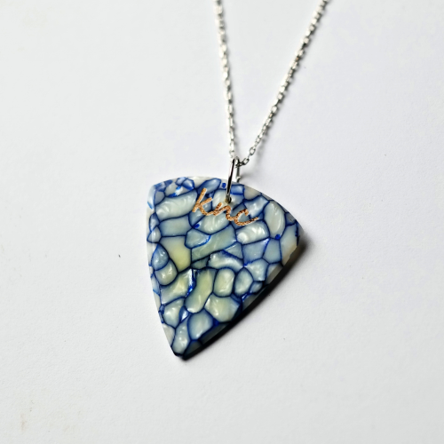 A personalized Blue Galalith pick on a necklace, showing a custom name laser-engraved on the pearlescent surface.
