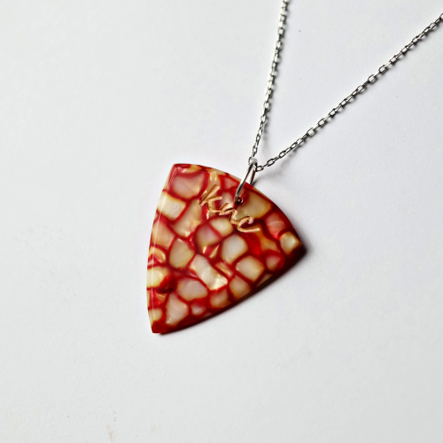 A personalized Red Galalith pick on a necklace, showing a custom name laser-engraved on the pearlescent surface.