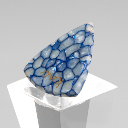 A Knc Picks handmade guitar pick made from Blue Galalith (Casein), showing the vibrant, pearlescent blue swirl patterns.