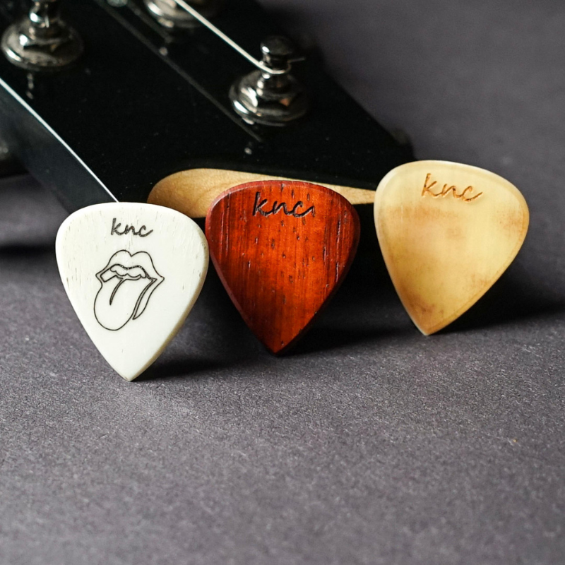 A collection of Knc Picks custom guitar picks showing all available natural materials: wood, bone, horn, and galalith.