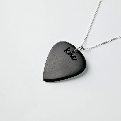 A handmade Knc Picks Ebony wood guitar pick, showing its pure black color, attached to a durable necklace chain.