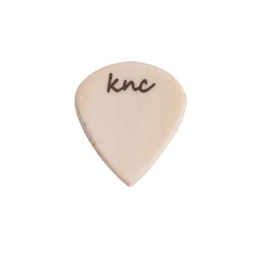 A Knc Picks handmade 'Lil One' (Jazz-style) guitar pick, crafted from natural bone, highlighting its small, sharp shape.