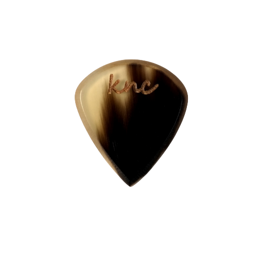 A Knc Picks handmade 'Lil One' (Jazz-style) guitar pick, crafted from natural variegated horn, highlighting its small, sharp shape.