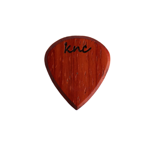 A Knc Picks handmade 'Lil One' (Jazz-style) guitar pick, crafted from vibrant reddish-orange Padouk wood, highlighting its small, sharp shape.