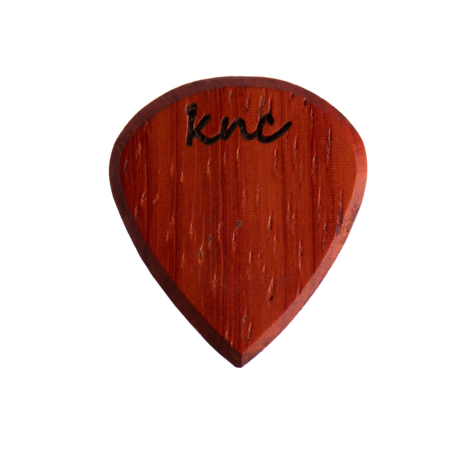 A Knc Picks handmade 'Lil One' (Jazz-style) guitar pick, crafted from vibrant reddish-orange Padouk wood, highlighting its small, sharp shape.