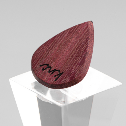 A Knc Picks handmade 'Lil One' (Jazz-style) guitar pick, crafted from vibrant natural Purpleheart wood, highlighting its small, sharp shape.