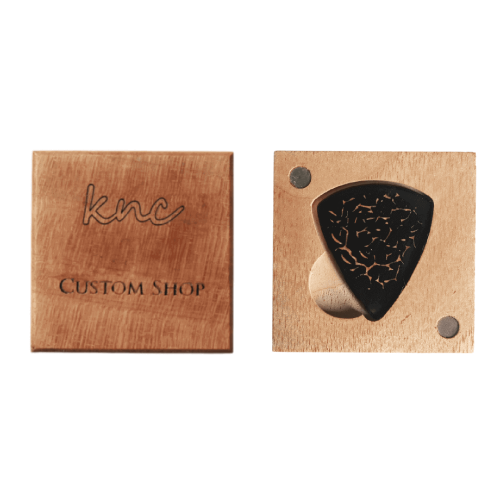 A handmade Knc Picks horn pick, laser-engraved with a 'Magma' (flowing lava) design, shown inside its included premium wooden gift box.