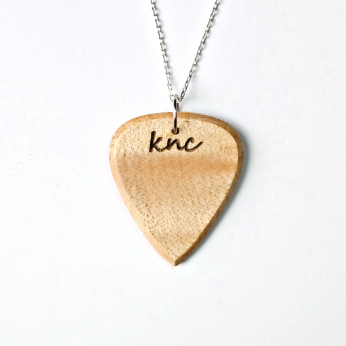 A handmade Knc Picks Maple wood guitar pick, showing its light color, attached to a durable necklace chain.