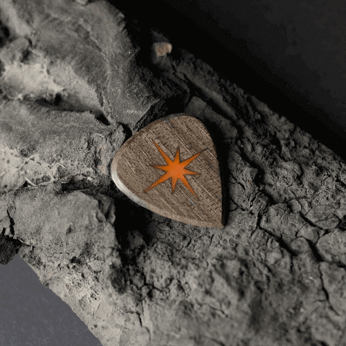 A handmade Knc Picks walnut wood guitar pick, laser-engraved with a 'Morning Star' (Çoban Yıldızı) logo that glows in the dark.