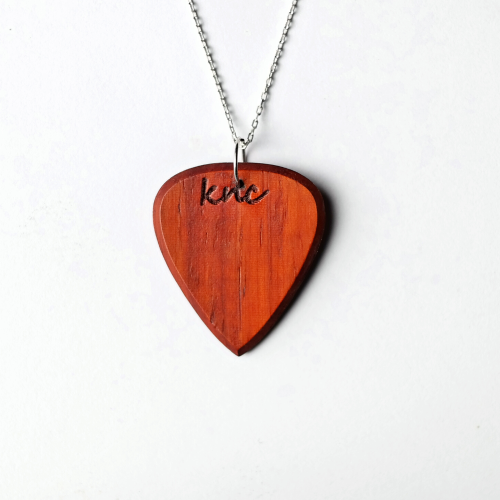 A handmade Knc Picks Padouk wood guitar pick (reddish-orange color) attached to a premium Silver necklace chain.