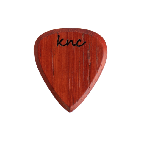 A handmade Knc Picks guitar pick crafted from natural Padouk (Paduk) wood, showing its deep reddish-orange color.
