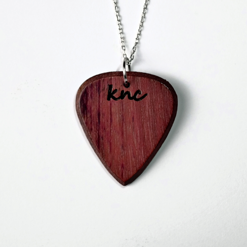 A handmade Knc Picks Purpleheart (Morkalp) wood guitar pick, showing its vibrant purple color, attached to a stylish necklace chain.