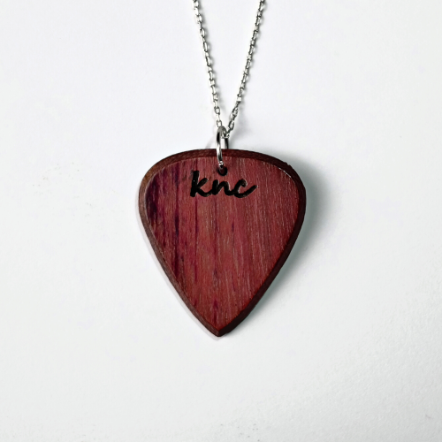 A handmade Knc Picks Purpleheart (Morkalp) wood guitar pick, showing its vibrant purple color, attached to a stylish necklace chain.