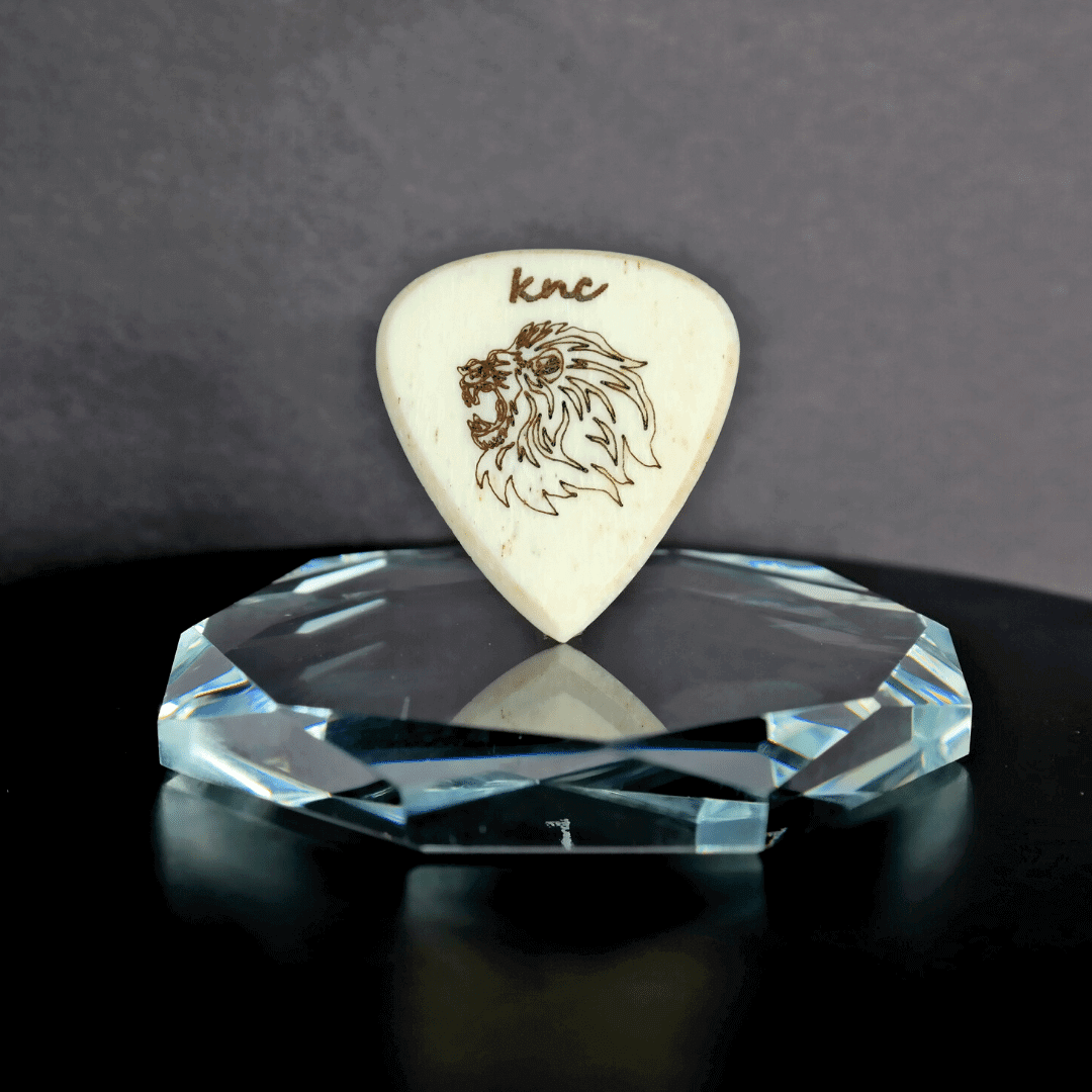 A Knc Picks handmade 2.0mm bone guitar pick from the Wild Life Series, featuring a detailed, laser-engraved Roaring Lion design.