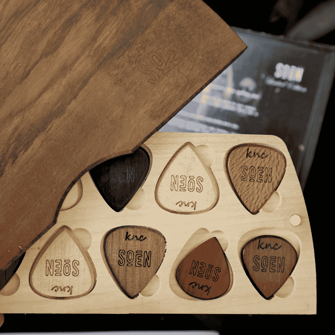 An arrangement of the 10 different natural material guitar picks from the SOEN signature set, showing various wood grains and horn textures.