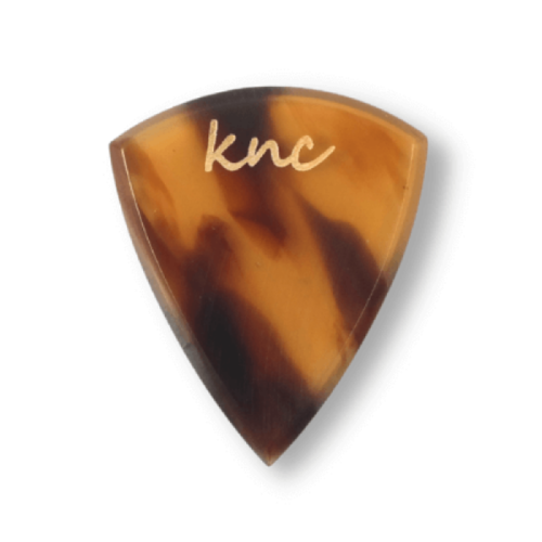 A Knc Picks handmade guitar pick made from 'Tortoise Shell' (Bağa) Galalith (Casein), showing the classic brown, amber, and yellow pattern.