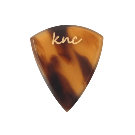 A Knc Picks handmade guitar pick made from 'Tortoise Shell' (Bağa) Galalith (Casein), showing the classic brown, amber, and yellow pattern.