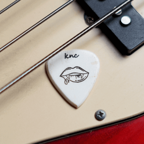 A handmade custom bone guitar pick featuring a laser-engraved vampire logo, shown on a dark, moody background.