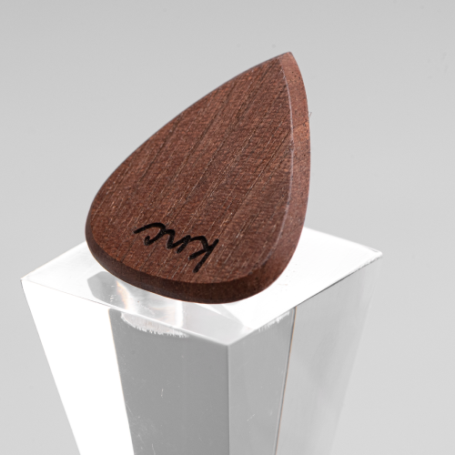 A handmade Knc Picks guitar pick crafted from natural Walnut wood, showing its deep, dark grain structure.