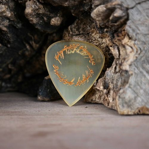 Close-up macro detail of the 'Ring of Power' script engraving on a polished natural horn guitar pick.