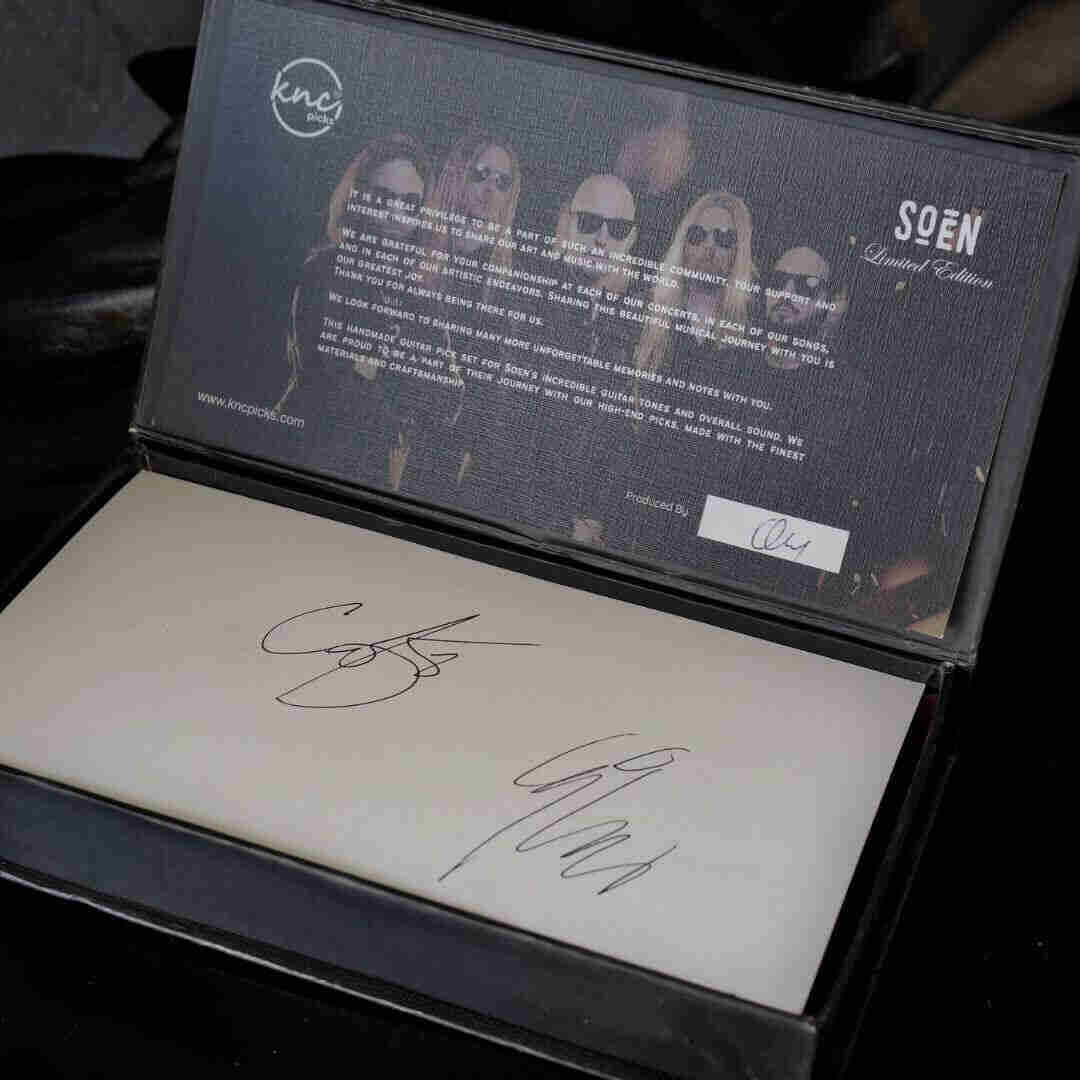 A close-up of the wooden box for the SOEN pick set, showing the authentic signatures of band members Cody Ford and Lars Åhlund