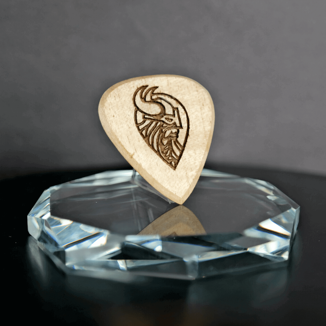 The Knc Picks Viking Shield engraved maple guitar pick showing the wood grain and design.